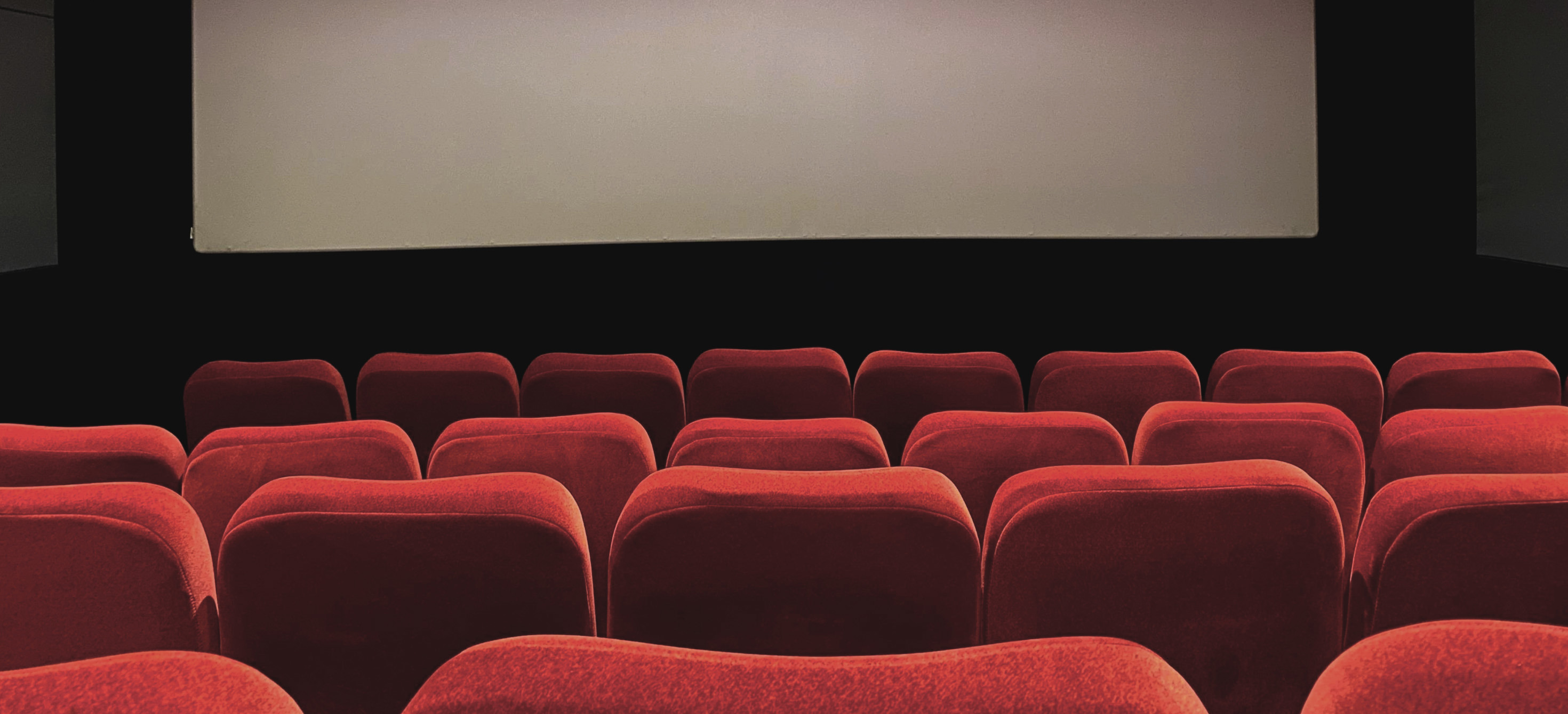 A movie theatre screen with red velvet seats