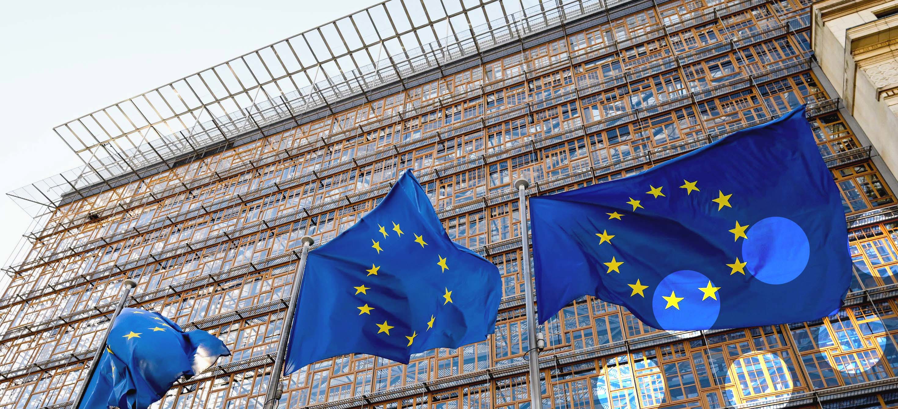 Three large EU flags flutter outside of an institutional building.