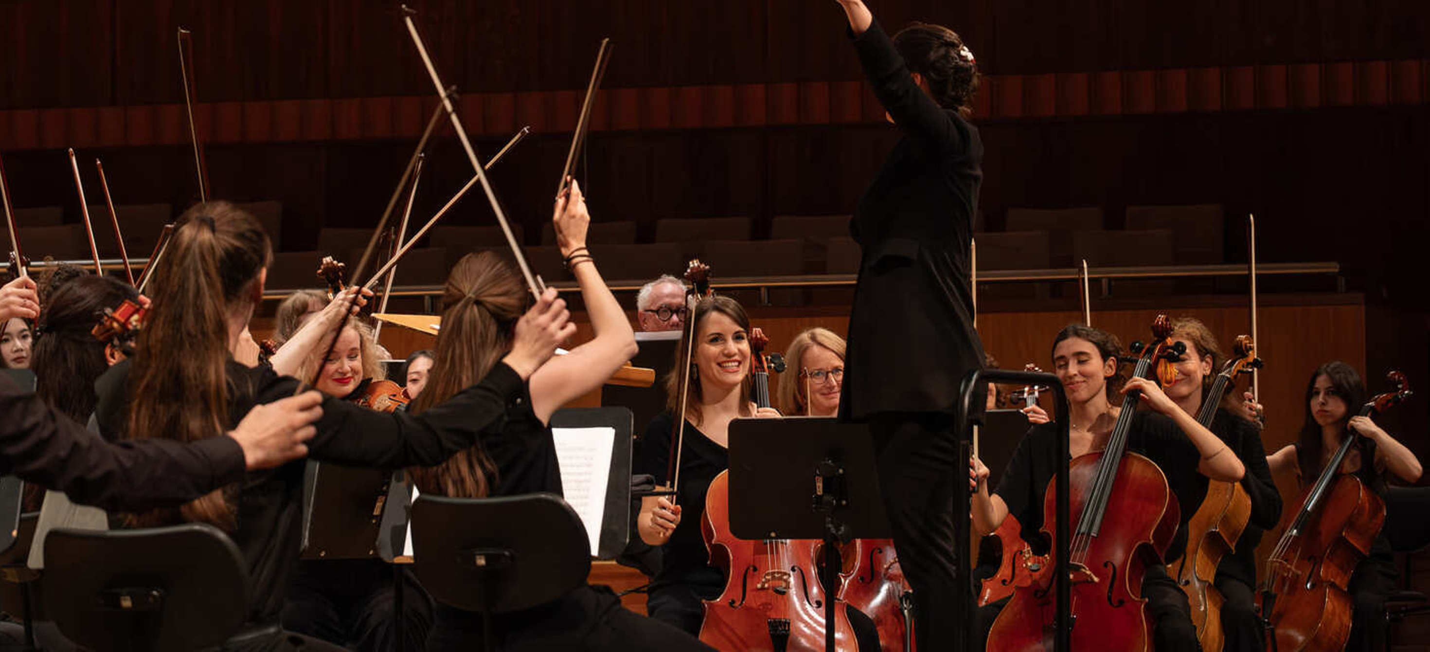 Image of an orchestra string section surrounding the conductor in a theatre